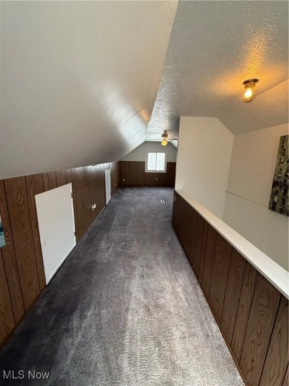 Bonus room with lofted ceiling, dark colored carpet, a textured ceiling, and wooden walls