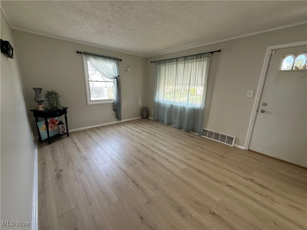 Unfurnished living room featuring wood finished floors, a textured ceiling, and ornamental molding
