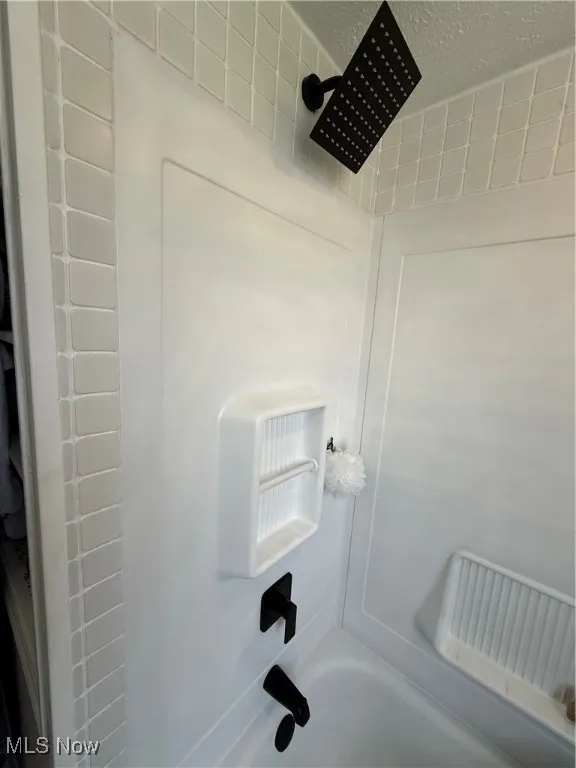 Bathroom view of washtub / shower combination and a textured ceiling