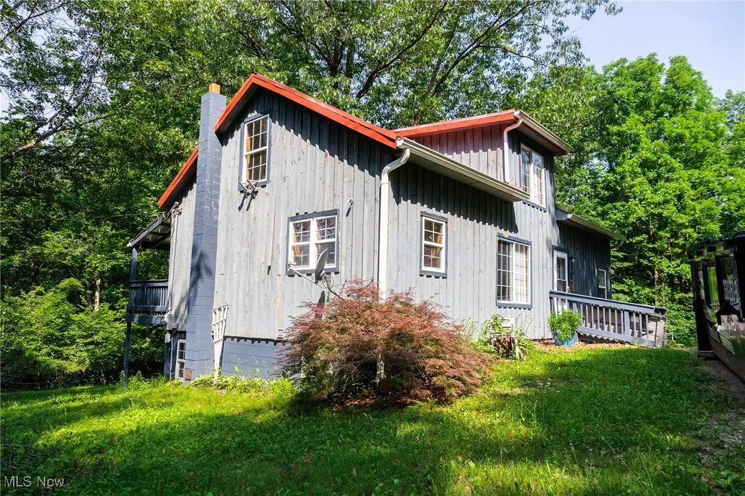 View of side of property featuring board and batten siding, a chimney, and a lawn