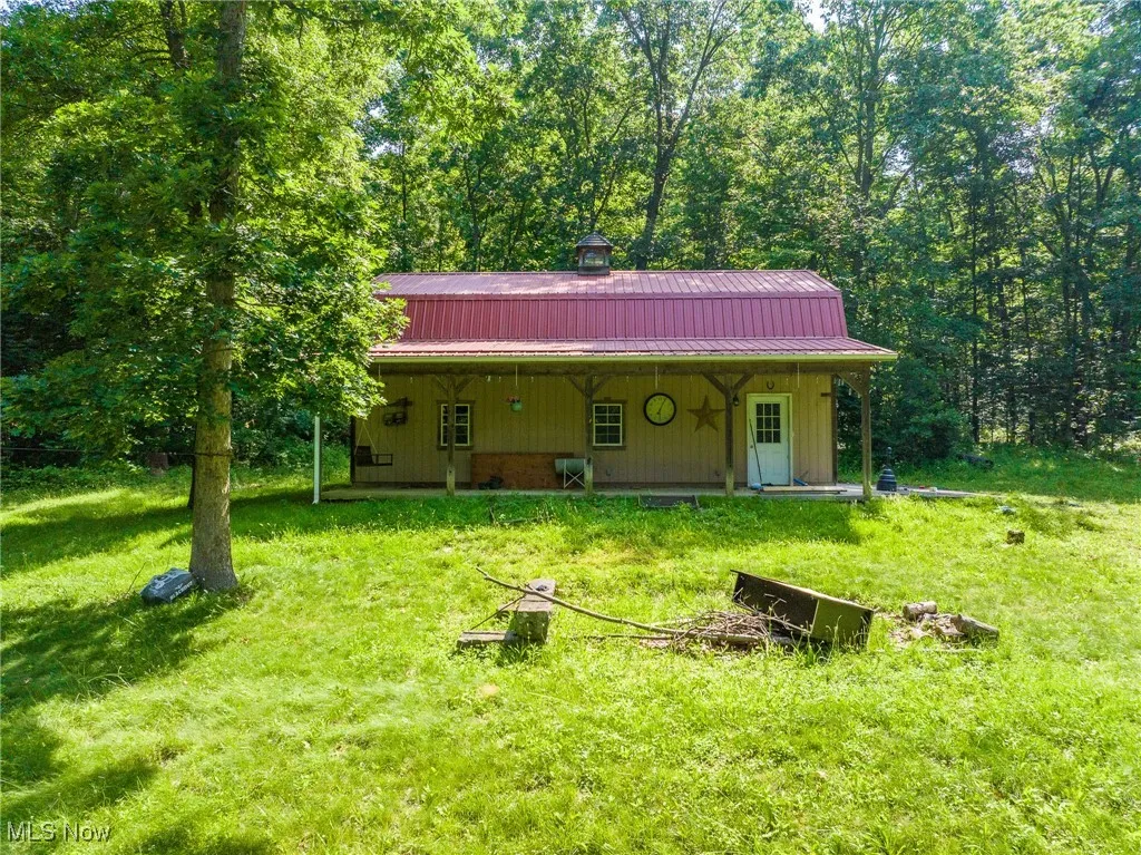 View of front facade with a metal roof, a front lawn, and a wooded view