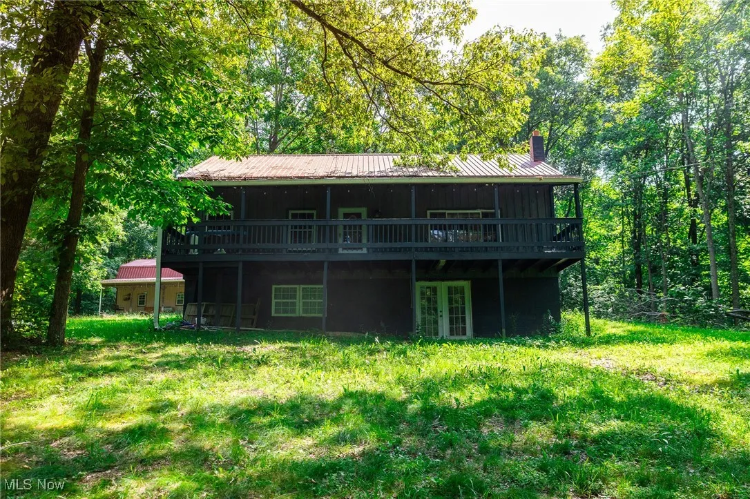 Rear view of house featuring french doors, a wooden deck, a chimney, a metal roof, and a lawn