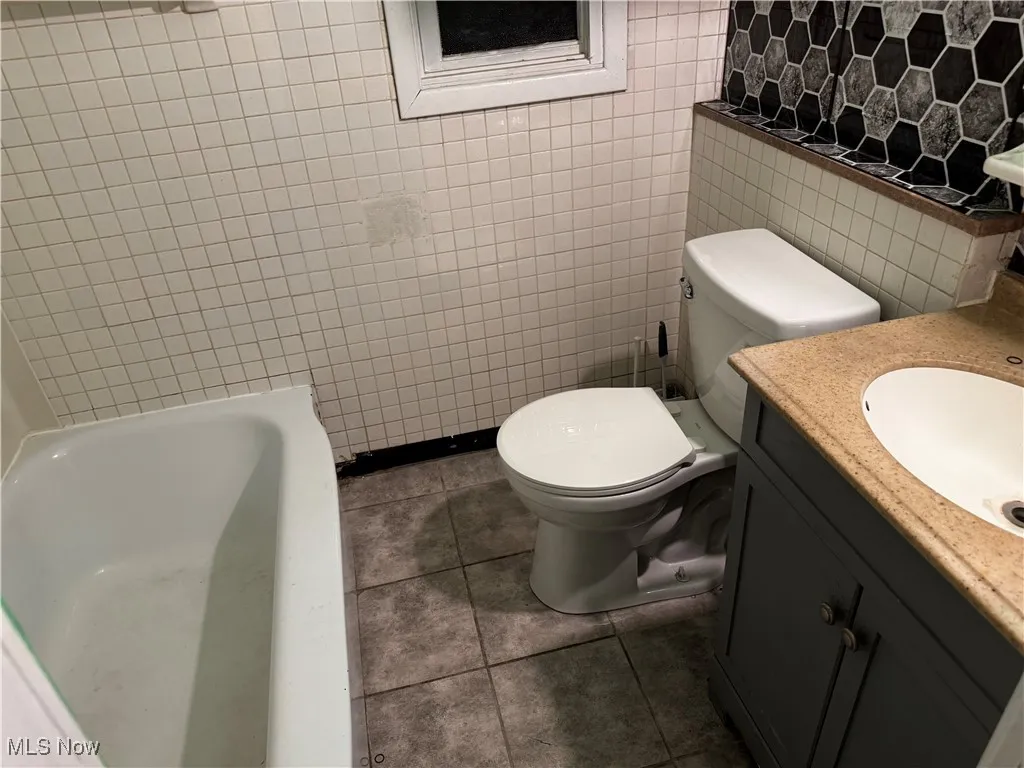 Full bathroom featuring vanity, a bathtub, tile walls, and tile patterned flooring