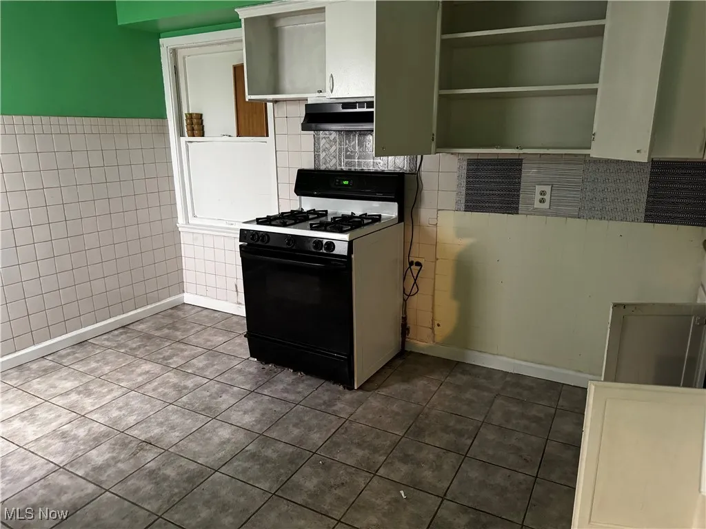 Kitchen featuring gas range, dark tile patterned flooring, open shelves, tile walls, and under cabinet range hood