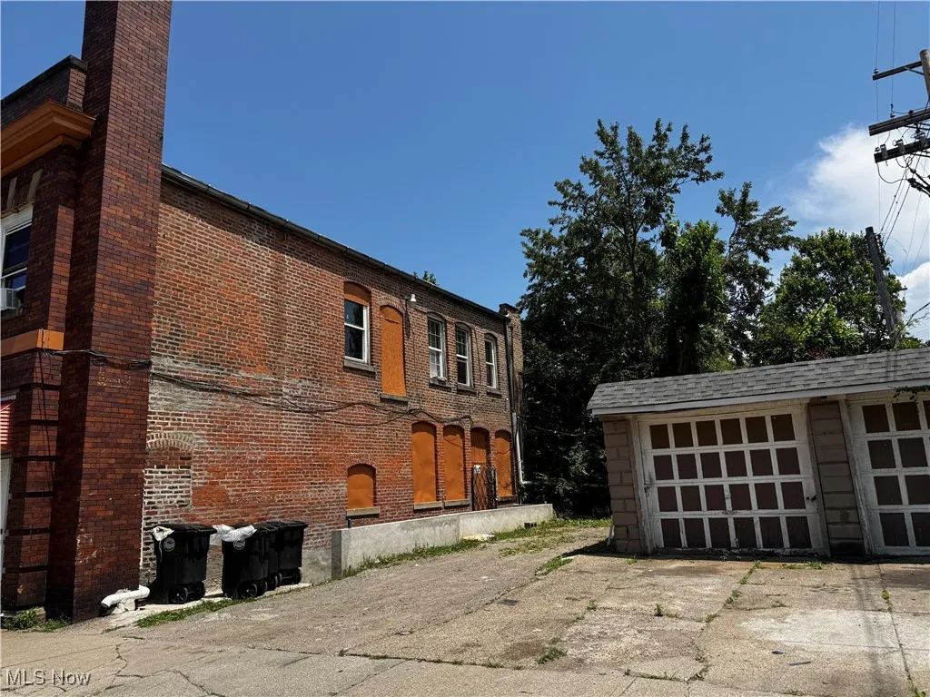 View of property exterior featuring brick siding, driveway, a chimney, and an outbuilding