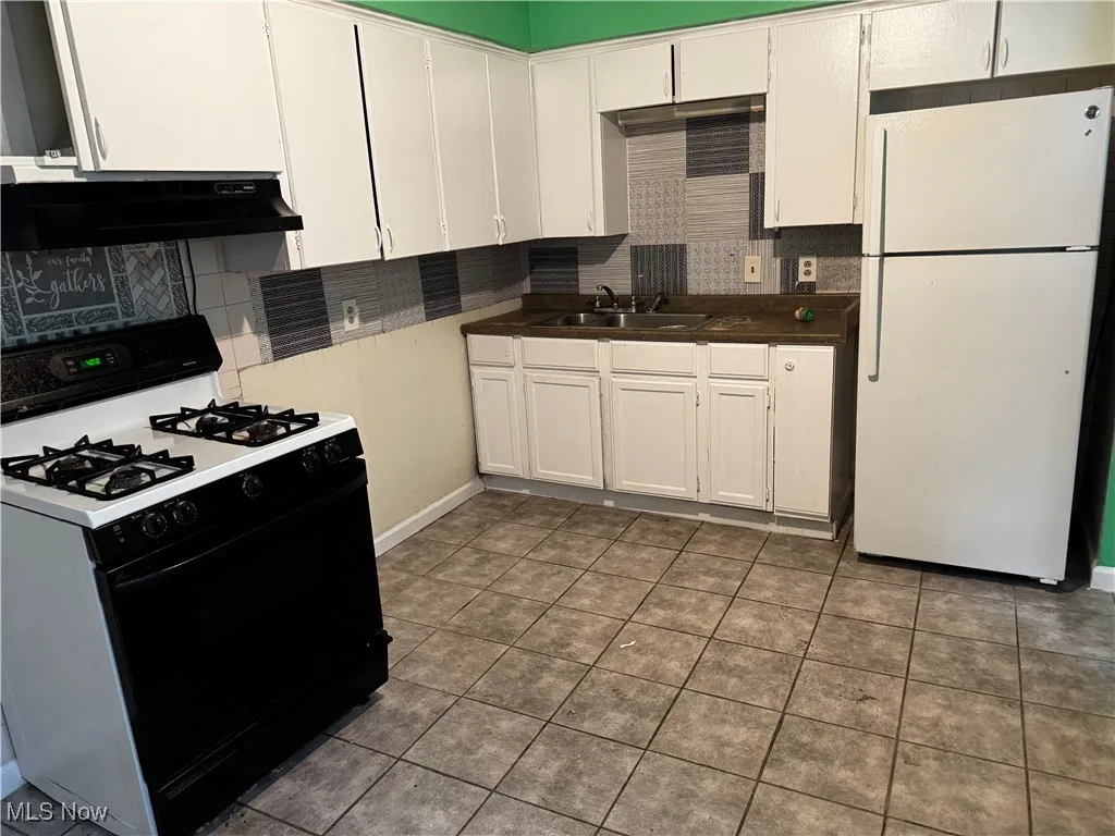 Kitchen with gas range oven, freestanding refrigerator, backsplash, and white cabinets