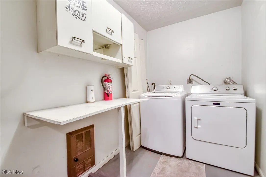 Washroom with cabinet space, washer and clothes dryer, and a textured ceiling