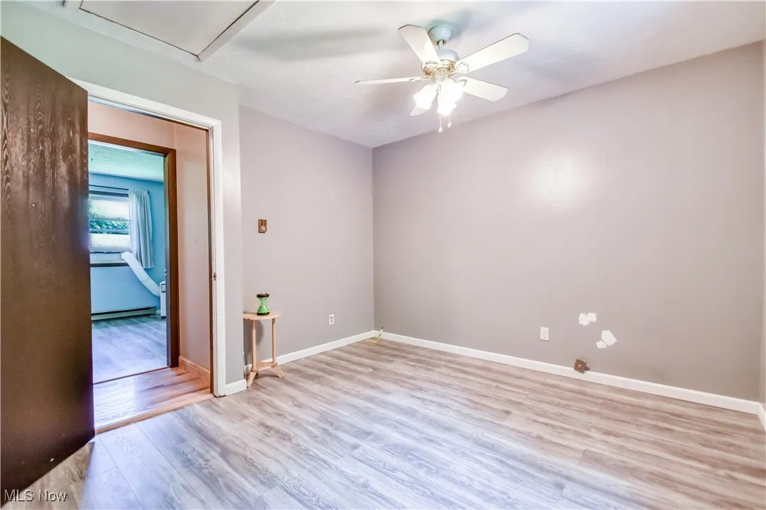 Unfurnished room with light wood-style floors, ceiling fan, and a baseboard heating unit