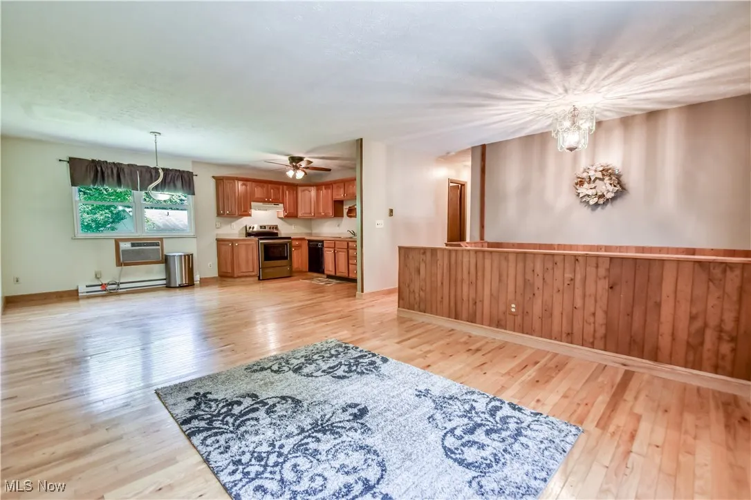 Unfurnished living room featuring light wood-style floors, a chandelier, a ceiling fan, a wall unit AC, and a baseboard heating unit