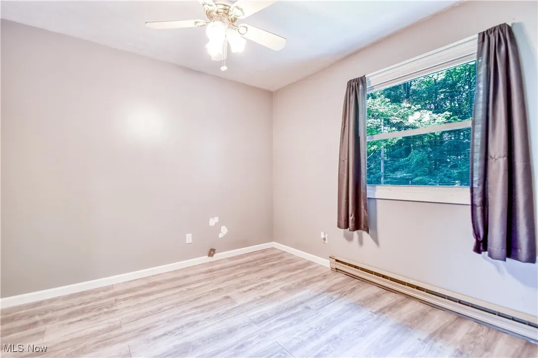 Unfurnished room with a baseboard heating unit, wood finished floors, and a ceiling fan
