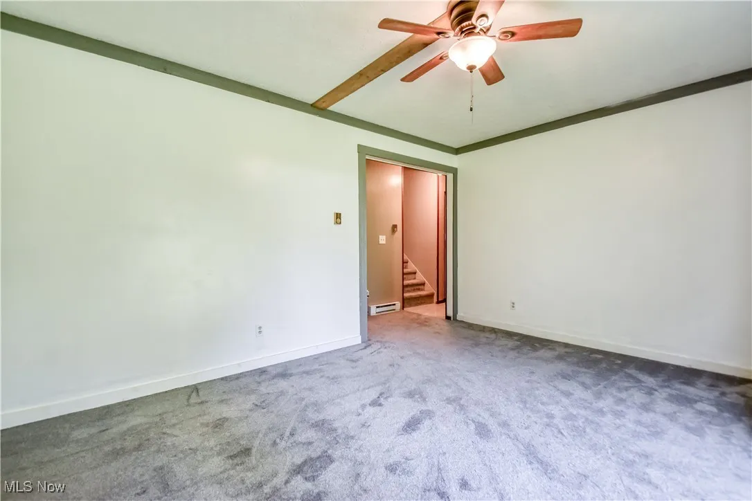 Spare room with carpet, ceiling fan, stairs, and a baseboard heating unit