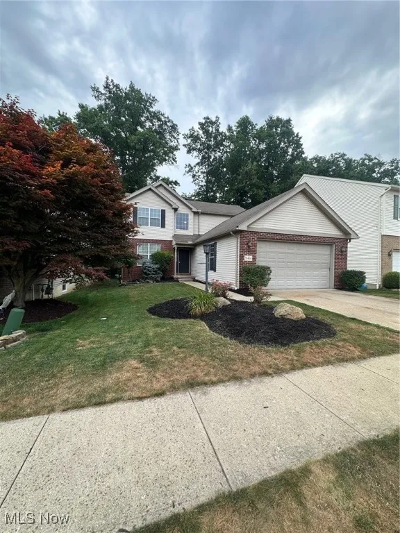 Traditional-style home featuring brick siding, driveway, a garage, and a front lawn