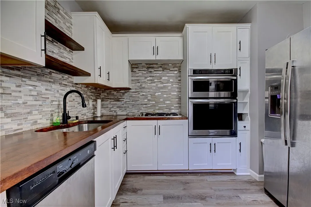 Kitchen with stainless steel appliances, light wood finished floors, white cabinets, tasteful backsplash, and butcher block counters