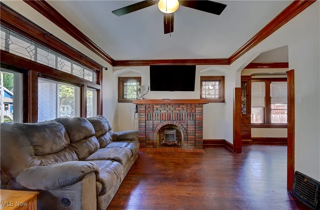 Living area featuring crown molding, healthy amount of natural light, a fireplace, wood finished floors, and ceiling fan