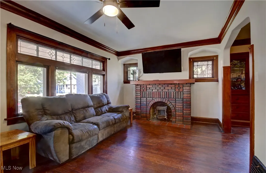 Living room featuring ornamental molding, wood finished floors, a ceiling fan, and a fireplace