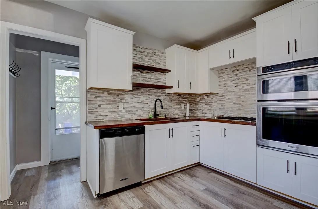 Kitchen featuring wood counters, open shelves, appliances with stainless steel finishes, light wood-style flooring, and decorative backsplash