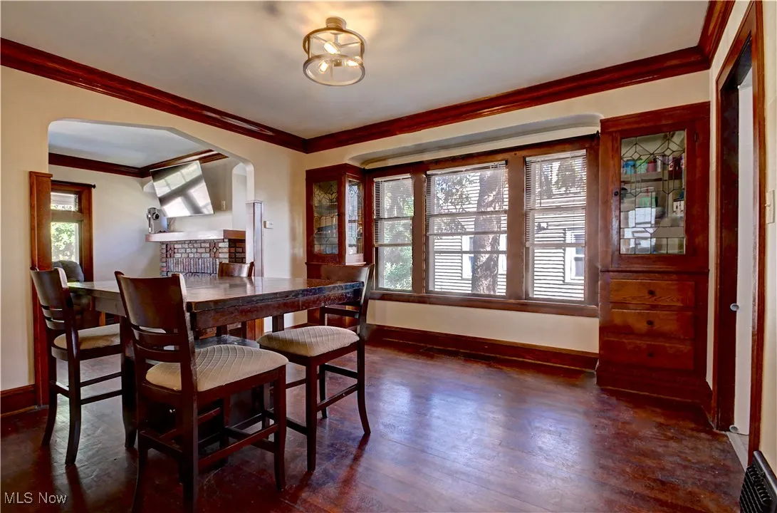 Dining space with arched walkways, ornamental molding, and wood finished floors