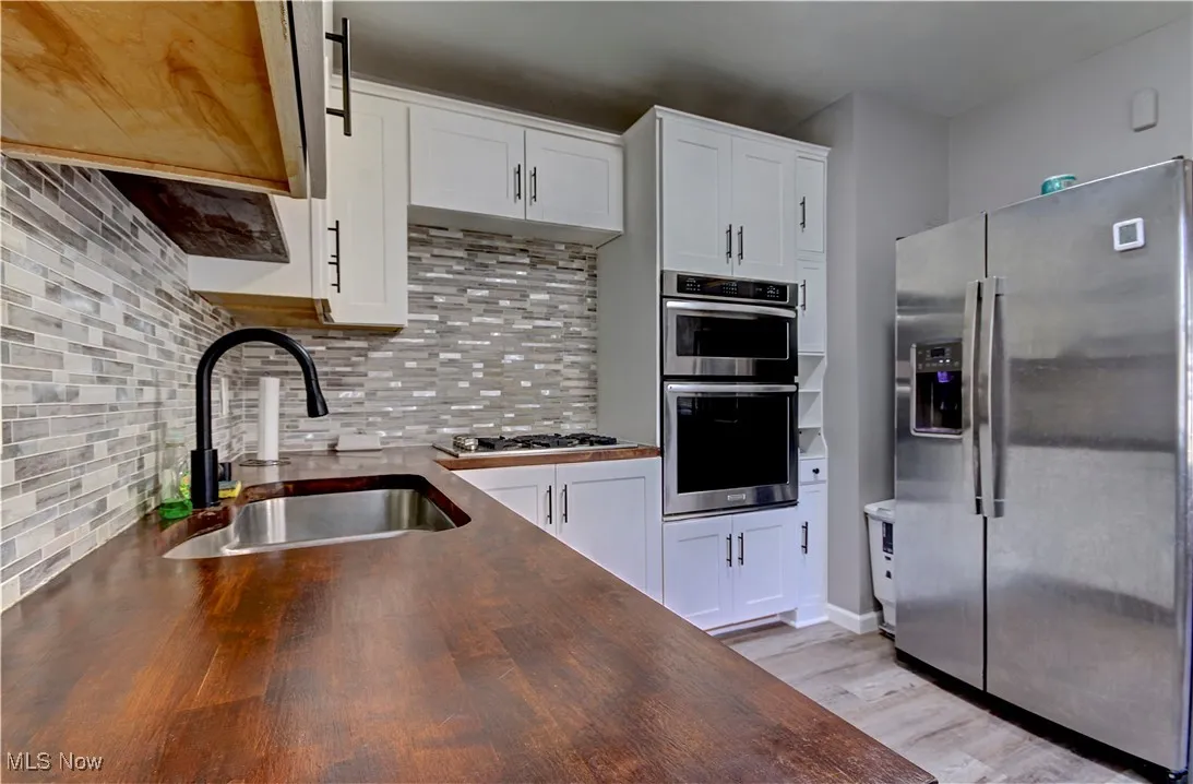 Kitchen featuring wooden counters, stainless steel appliances, backsplash, light wood-style flooring, and white cabinets
