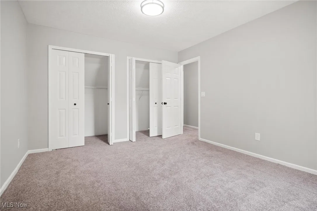 Unfurnished bedroom with two closets, carpet flooring, and a textured ceiling
