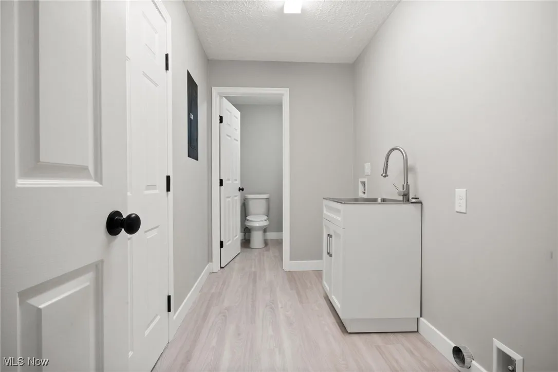 Washroom with a textured ceiling, light wood-type flooring, and cabinet space