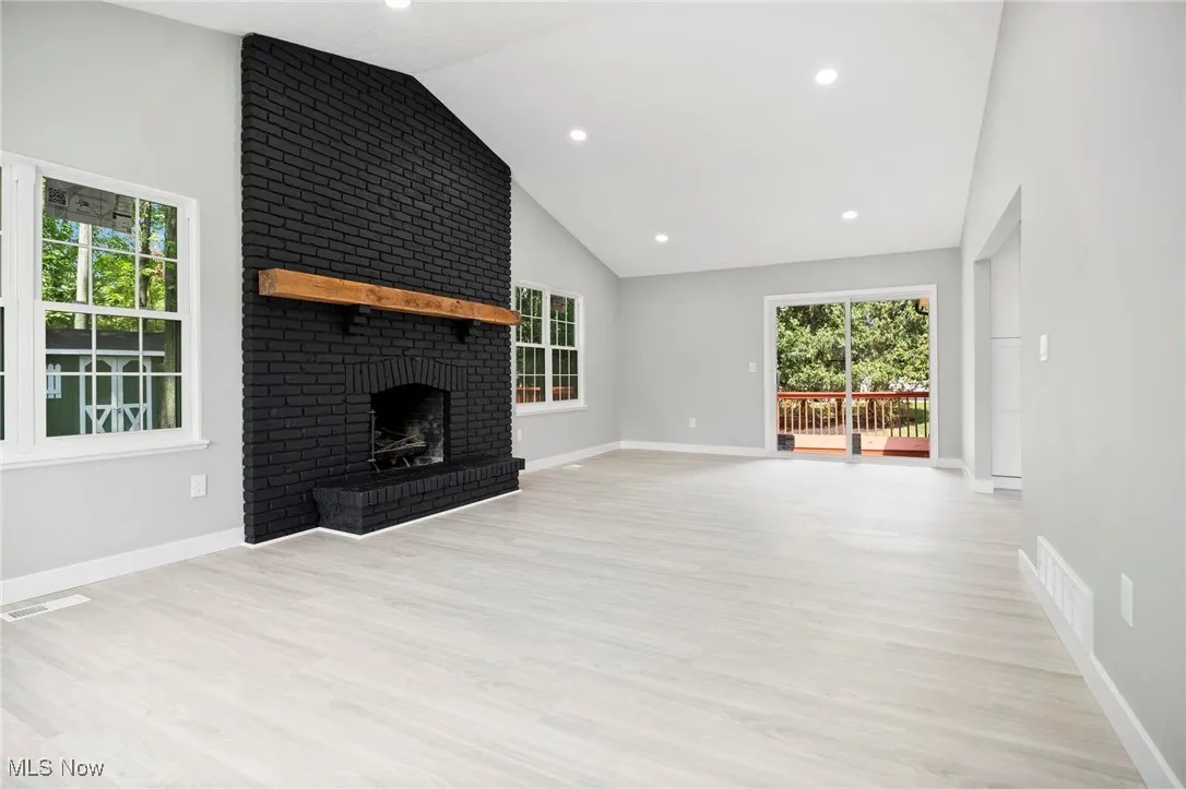 Unfurnished living room with light wood-style floors, a brick fireplace, recessed lighting, and high vaulted ceiling