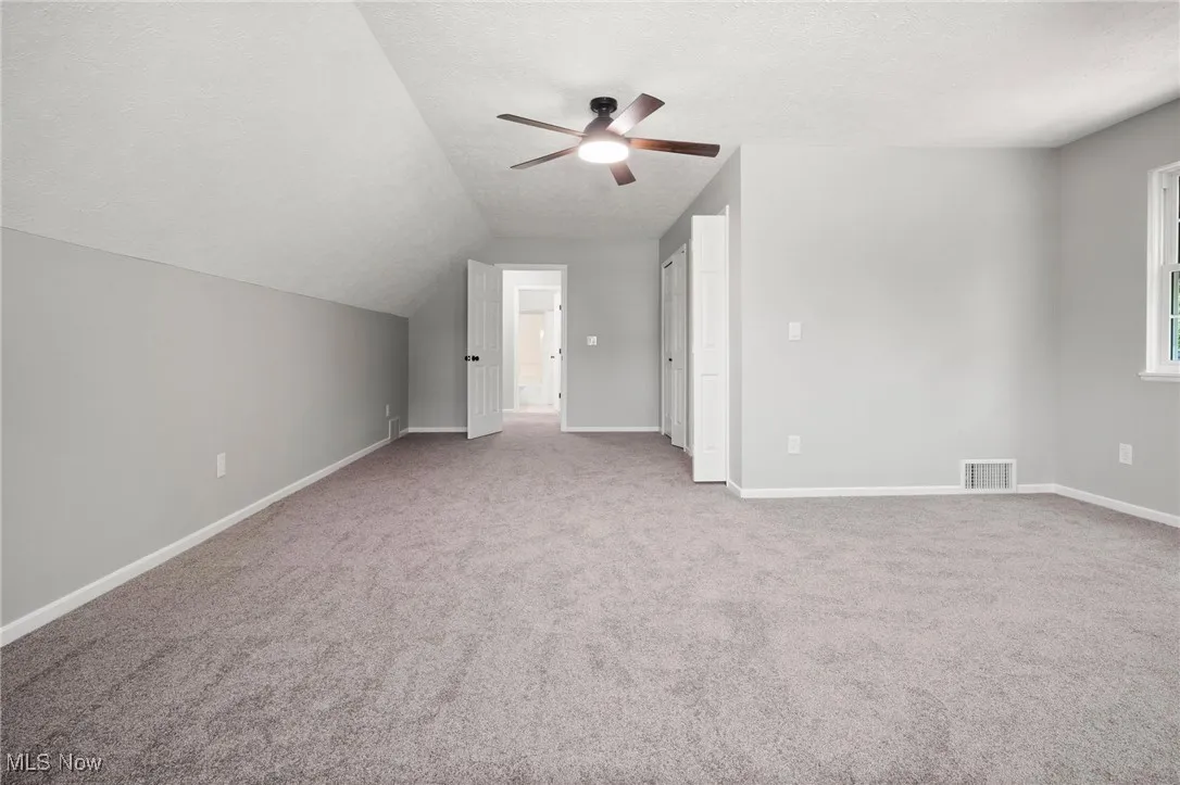 Additional living space with ceiling fan, carpet, vaulted ceiling, and a textured ceiling