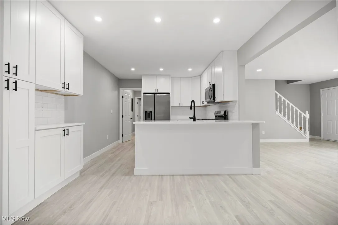 Kitchen with backsplash, white cabinetry, light wood finished floors, stainless steel appliances, and recessed lighting