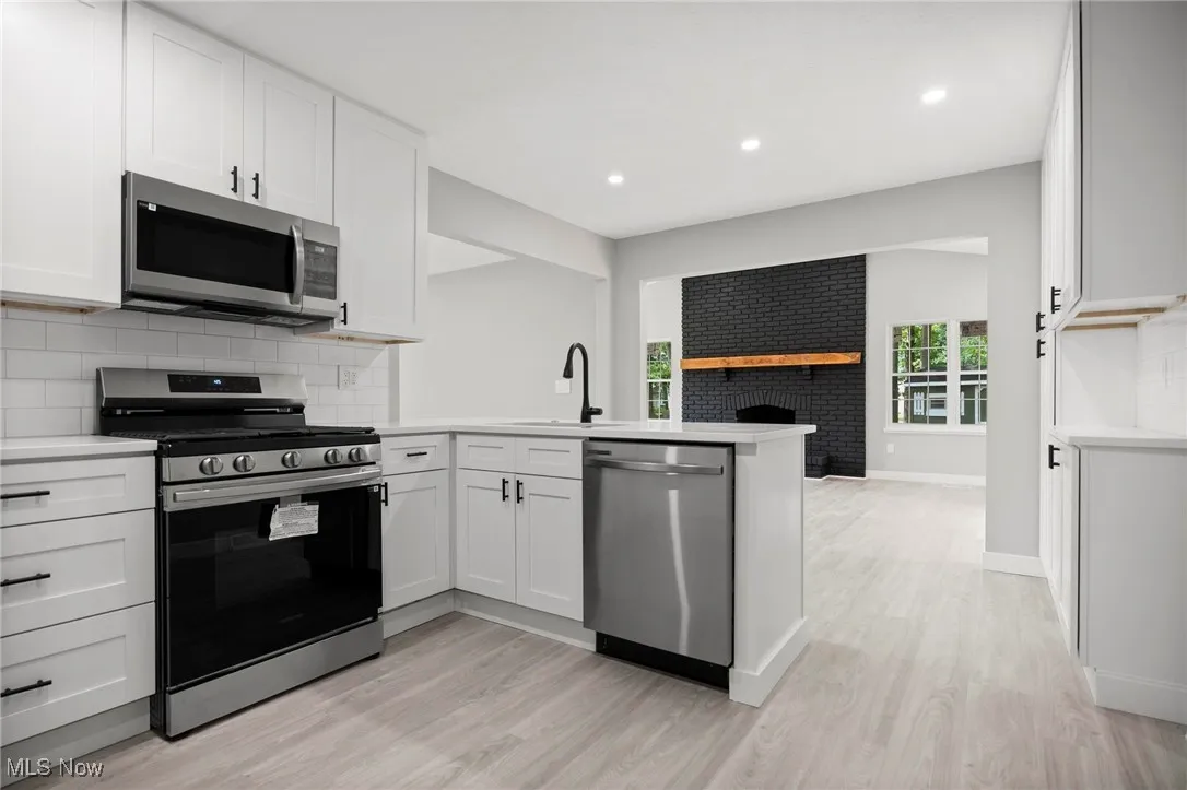 Kitchen with decorative backsplash, stainless steel appliances, open floor plan, white cabinetry, and light wood finished floors