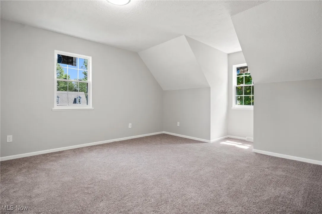 Additional living space with vaulted ceiling, carpet flooring, and a textured ceiling