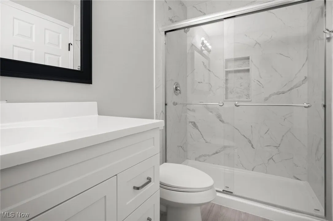 Full bath featuring vanity, a marble finish shower, and wood finished floors