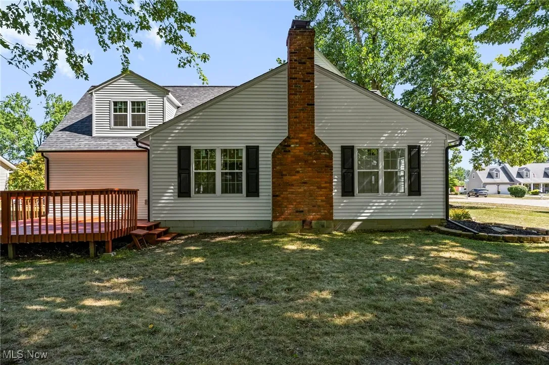Rear view of property with a shingled roof, a wooden deck, a lawn, and a chimney