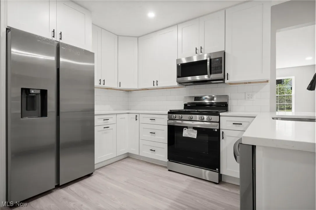 Kitchen with appliances with stainless steel finishes, backsplash, light wood-type flooring, white cabinets, and recessed lighting