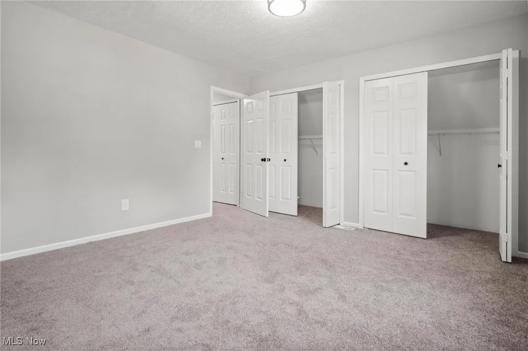 Unfurnished bedroom with multiple closets, carpet flooring, and a textured ceiling