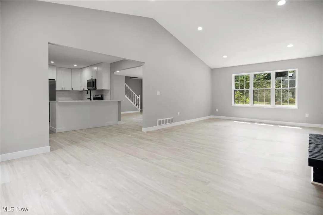 Unfurnished living room with vaulted ceiling, recessed lighting, light wood-style flooring, and stairway