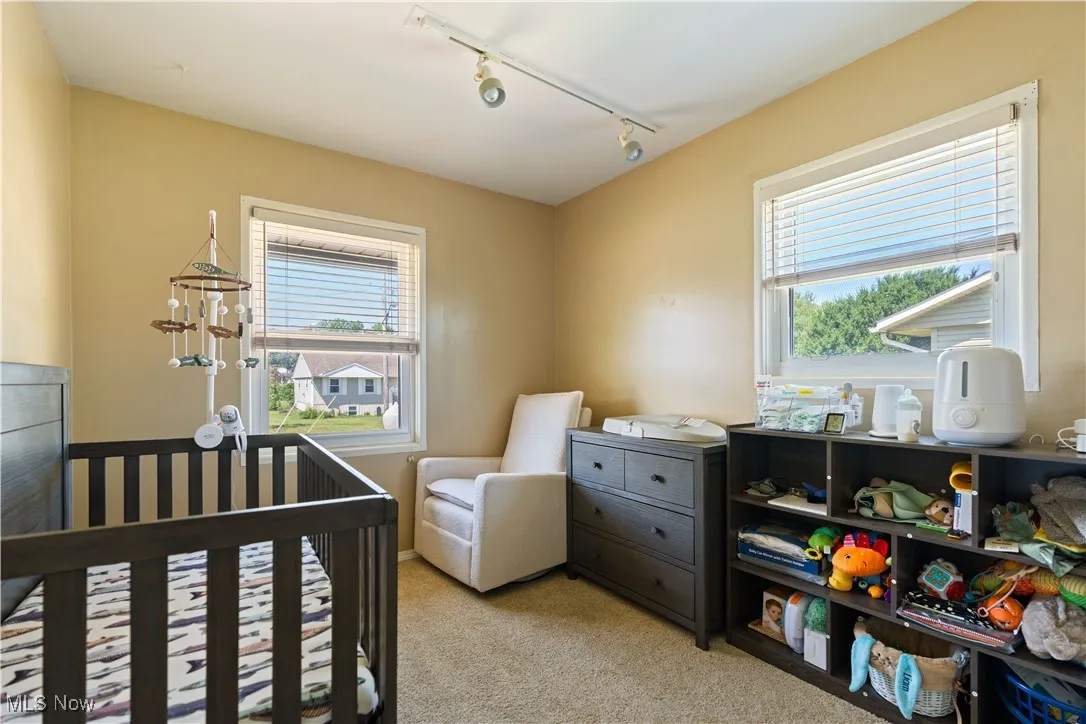 Bedroom featuring rail lighting, light colored carpet, and a crib