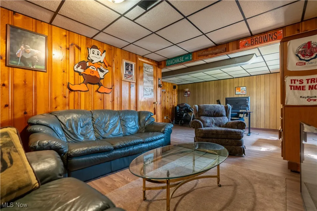 Living area featuring a drop ceiling, wooden walls, and wood finished floors