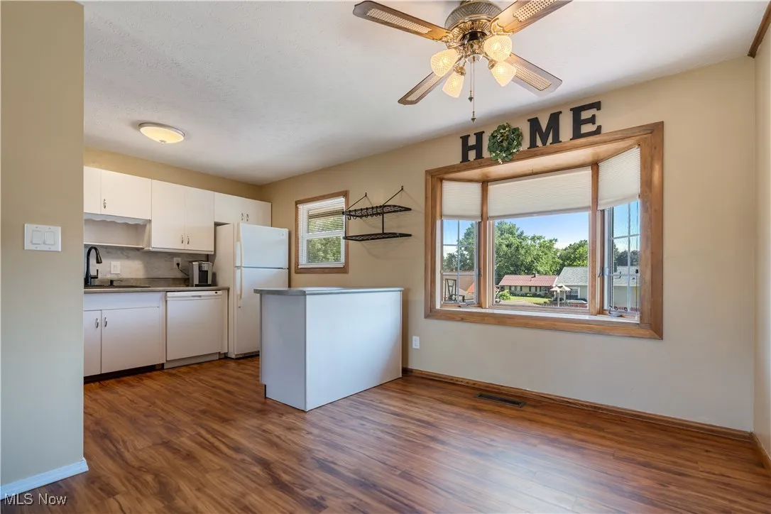 Kitchen with white cabinets, dark wood-style floors, white appliances, and ceiling fan