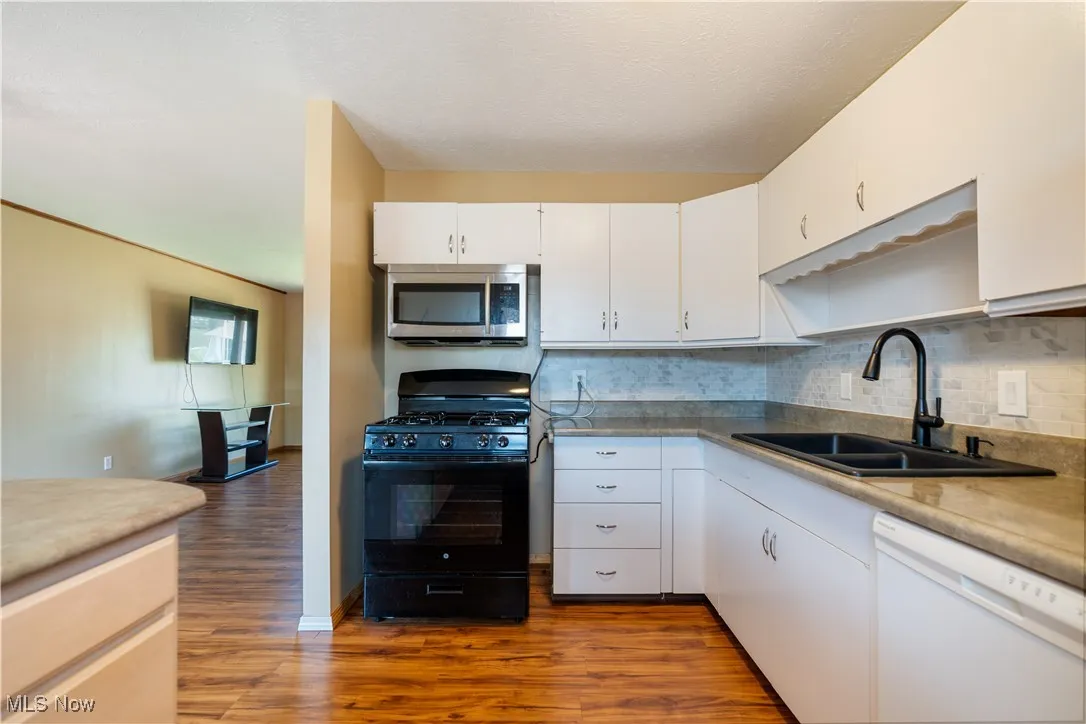 Kitchen featuring black gas range oven, white dishwasher, stainless steel microwave, dark wood-style flooring, and decorative backsplash