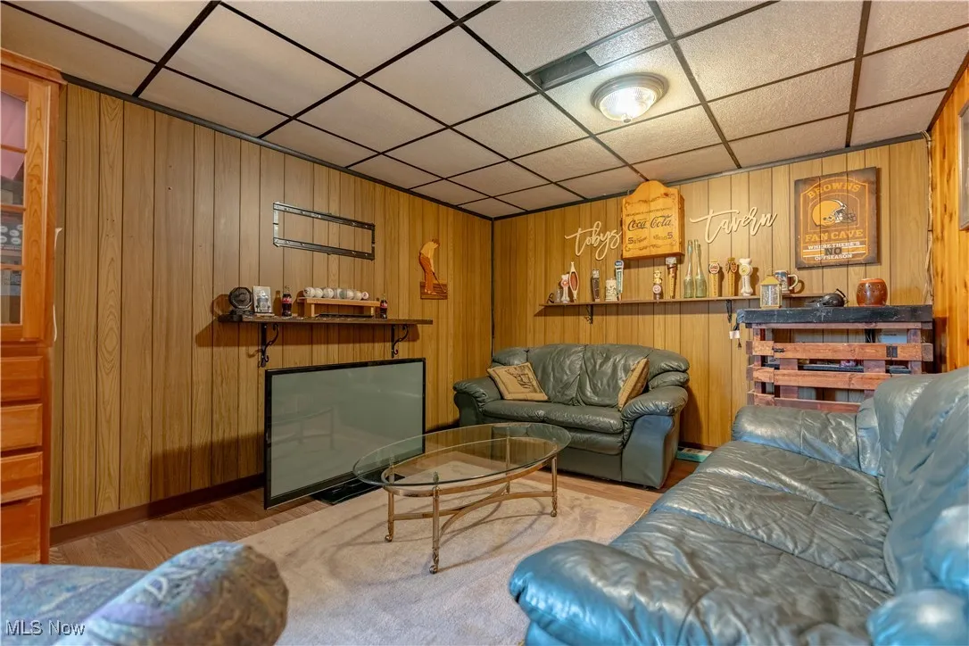 Living room featuring a paneled ceiling, wood finished floors, and wooden walls