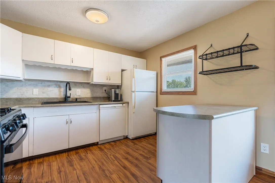 Kitchen with white appliances, dark wood-style floors, white cabinetry, and decorative backsplash