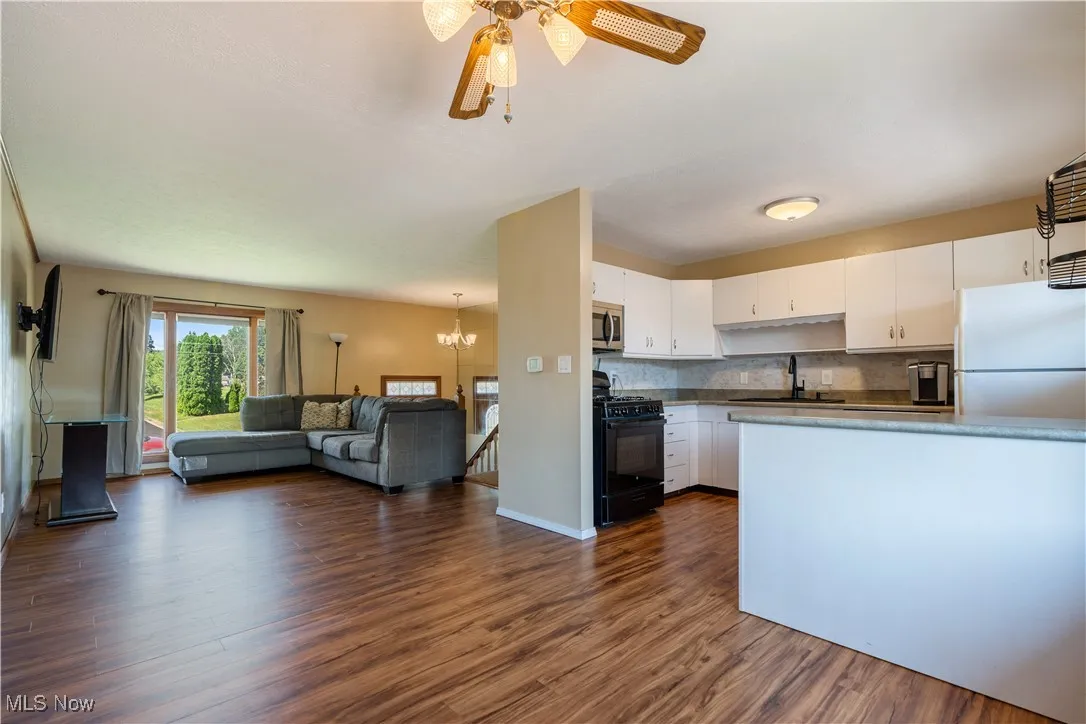 Kitchen with open floor plan, black gas range oven, freestanding refrigerator, dark wood-type flooring, and white cabinetry