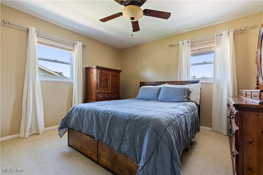 Bedroom with light carpet, multiple windows, and ceiling fan