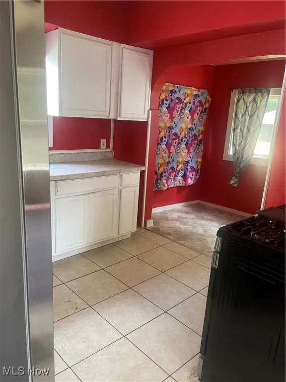 Kitchen featuring stainless steel stove, white cabinets, light countertops, and refrigerator