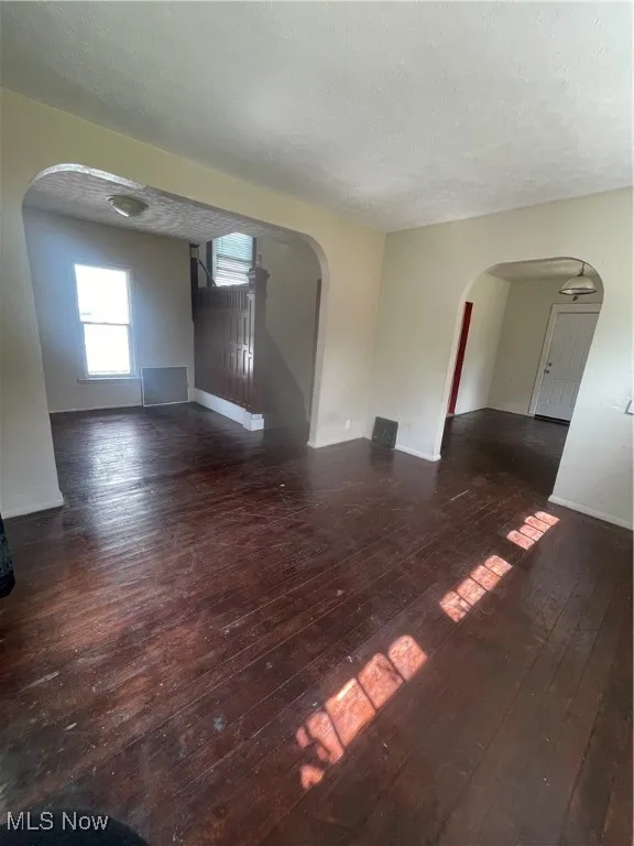 Unfurnished living room featuring arched walkways, a textured ceiling, and dark wood finished floors