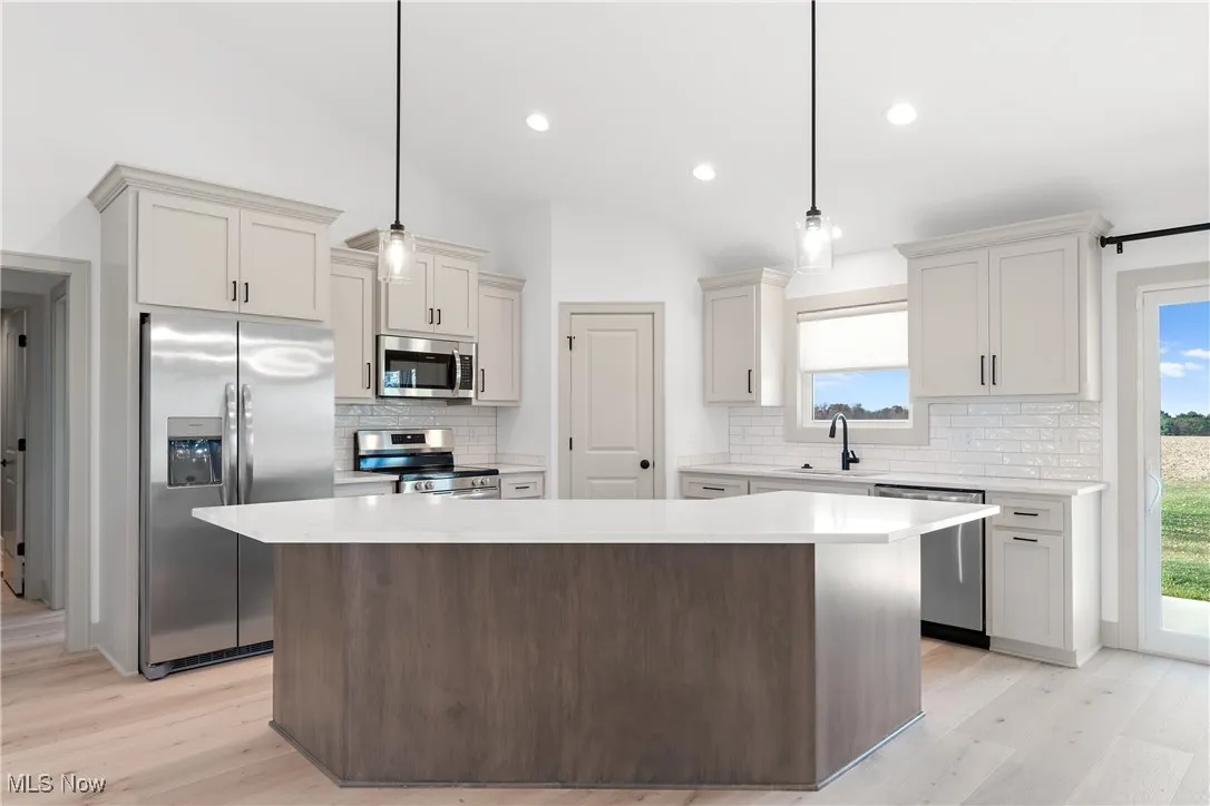 Kitchen featuring a center island, lofted ceiling, decorative backsplash, and stainless steel appliances