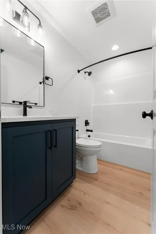 Full bathroom with toilet, vanity, wood-type flooring, and bathing tub / shower combination