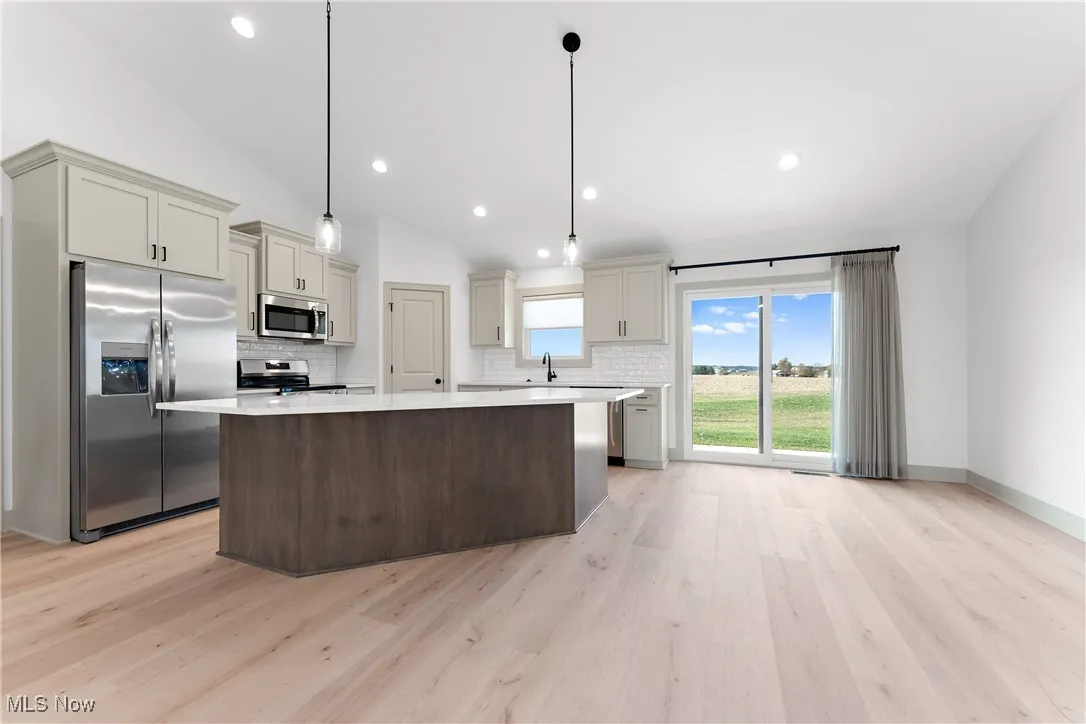 Kitchen featuring stainless steel appliances, decorative light fixtures, light hardwood / wood-style flooring, a center island, and vaulted ceiling