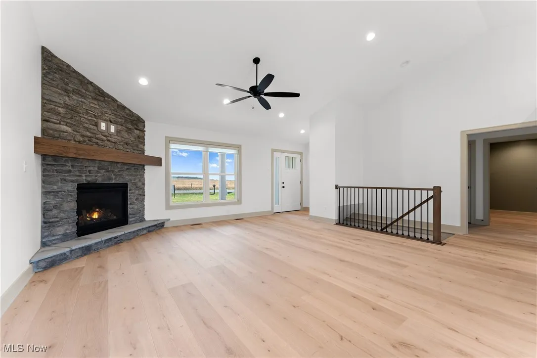 Unfurnished living room featuring a stone fireplace, light wood-type flooring, lofted ceiling, and ceiling fan