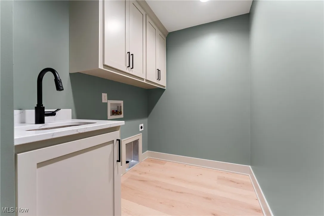 Clothes washing area with hookup for a washing machine, cabinets, sink, light hardwood / wood-style floors, and electric dryer hookup