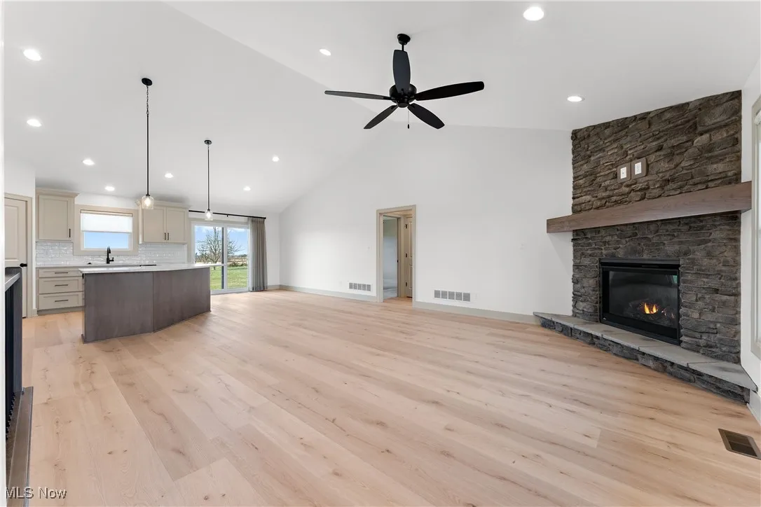 Unfurnished living room featuring light hardwood / wood-style floors, sink, ceiling fan, high vaulted ceiling, and a fireplace
